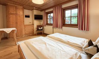 A cozy bedroom with wooden paneling and a large window. There are two single beds and a wardrobe.