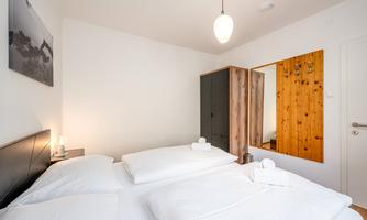 A bright bedroom with two beds and fresh bed linen. There is a wooden wardrobe and a mirror on the wall.