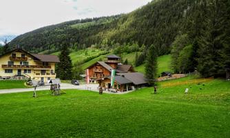 A picturesque landscape with green meadows and mountains in the background. In the foreground, there are several charming buildings and trees.
