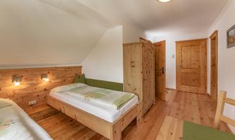 A cozy room with wooden furniture and two beds. The walls are light, and there is a wardrobe as well as a door to another room.