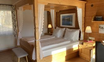 A cozy bedroom with a wooden canopy bed and light pillows. The warm wood paneling and soft lighting create an inviting atmosphere.