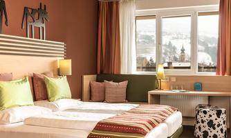 A modern hotel room with two beds and colorful cushions. Large windows offer a view of the snowy landscape.