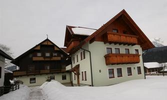 A cozy, two-story building with wooden cladding and balconies. Outside, snow covers the ground, and the sky is cloudy.