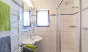 A modern bathroom with a shower, sink, and large tiles. Towels in green and gray colors are also visible.