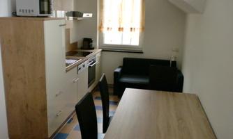 A modern kitchen corner with a dining table and chairs. The surroundings are bright and friendly with a windowsill and a cozy armchair.