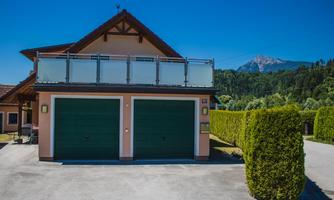 A modern house with green garage doors and a balcony. In the background, hills and a clear blue sky can be seen.