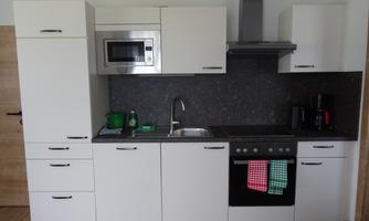 A modern kitchen with white cabinets and a dark countertop. It is equipped with appliances such as a stove, a microwave, and a coffee machine.