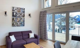 A modern living room with a purple sofa and a wooden table. Large windows offer a view of the mountains and the terrace.