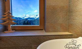 A bathroom with a view of the mountains and a window that shows the beautiful landscape. On the windowsill is a small wooden tree.