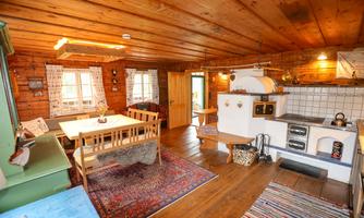 A cozy wooden cabin with a dining area and a small kitchen. The room is warm and inviting, featuring wooden paneling and a carpet.