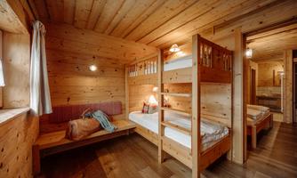 A cozy room with wooden paneling and bunk beds. There is a seating area and warm lighting for an inviting atmosphere.