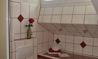 A small bathroom with white tiles and red accents. A sink, a toilet, and a window ensure brightness.