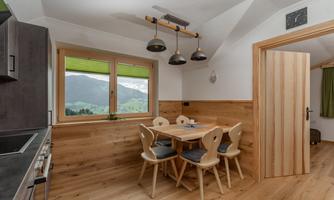 A cozy kitchen and dining area with a wooden table and chairs. The windows offer a beautiful view of the surrounding mountains.