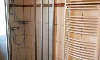 A bright bathroom with a modern shower cubicle and a towel warmer. The walls are tiled, giving the room a clean atmosphere.