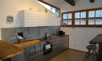 A modern kitchen with stainless steel fronts and an elegant white upper cabinet. Large windows provide plenty of light and a bright atmosphere.