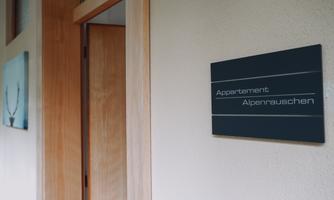 A hallway with a door to an apartment. On the wall hangs a sign with the inscription "Apartment Alpine Whisper."