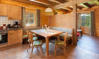 A cozy kitchen in rustic style with wood paneling. The dining table is set for four people, and large windows provide plenty of daylight.