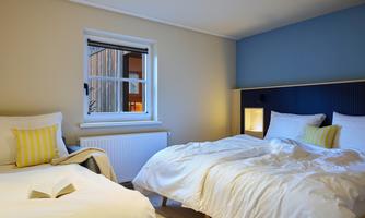A cozy bedroom with two beds and bright walls. A window lets in daylight.