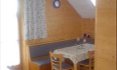 A cozy dining area with a table and chairs in a wooden decor. A window with curtains provides natural light.