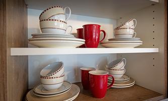 In the picture, dishes and cups are arranged on a shelf. There are white plates and red cups that match well together.