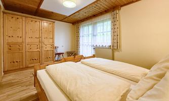 A cozy bedroom with two beds and wooden furniture. Large window with natural light and a view of the room.