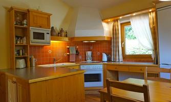 A bright kitchen with wooden cabinets and orange tiles. There is a stove, a microwave, and a dining area with a table and chairs.