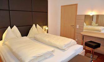 A modern bedroom with a double bed and elegant furnishings. The room features a mirror and a cozy chair.
