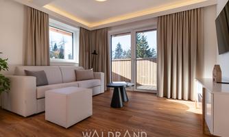 A modern living room with a comfortable sofa and a small table. Large windows provide plenty of daylight and a cozy atmosphere.