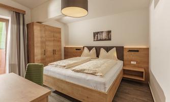 A modern bedroom with two beds and wooden details. The room is bright and friendly, with a desk and a large window.