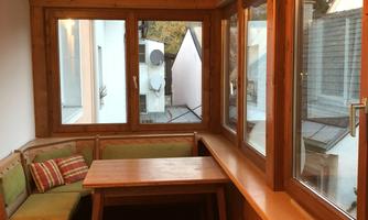 A cozy conservatory with wooden panels and large windows. A table and seating area invite you to relax.