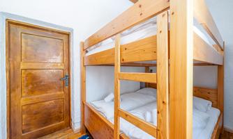 A bright bedroom with a wooden bunk bed. The door is made of wood and the floor is made of wood.
