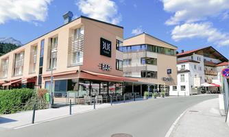 A modern building with a restaurant and a bar. The street is quiet and there are a few clouds in the blue sky.