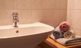A modern sink with a faucet and fluffy towels on a shelf. The walls are covered with bright tiles.