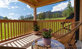 A cozy balcony with a view of green meadows and mountains. On the table stands a blooming plant, while the sun is shining.