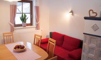 A cozy living space with a red sofa and a dining table. In the background, there is a plant on the windowsill and the room is brightly lit.