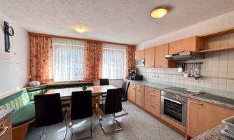 A modern kitchen with a cozy dining area and large windows. The wooden cabinets and the gray countertop give the kitchen an inviting atmosphere.