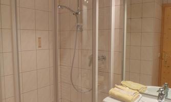 A modern bathroom with a glass shower and a white sink. Soft towels are ready, and the walls are tiled with light tiles.