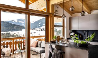 A modern kitchen with a view of snow-covered mountains. The space has large windows and a cozy atmosphere.