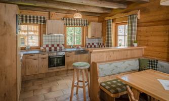 A cozy wooden room with a modern kitchen and a dining table. Large windows provide plenty of daylight and an inviting atmosphere.