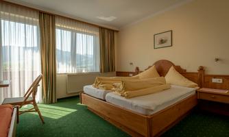 A cozy bedroom with a double bed and large windows. The decor is rustic and the floor is green with carpet.