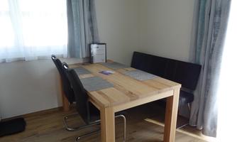 A cozy dining area with a wooden tray and black chairs. The large windows let in plenty of light.