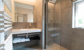 A modern bathroom with a glass shower and a white sink. Towels are neatly stacked and there is a large mirror.