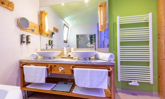 A modern bathroom with two sinks and a large mirror. The walls are painted in fresh colors and there is a towel warmer.