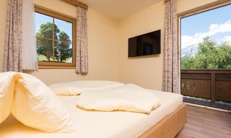 An inviting bedroom with a large window and a balcony. The room is bright and cheerful, equipped with a television and comfortable beds.