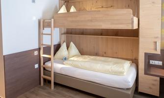 A modern bedroom with a bunk bed and a single bed. The room is bright and designed with wooden elements.