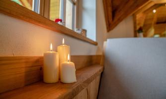 Three burning candles are standing on a wooden bench next to a window. The room has a warm and cozy atmosphere.