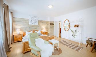 A bright bedroom with a cozy bed and modern furniture. There is an armchair and decorative elements on the wall.