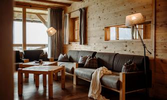 A cozy living space with wood paneling and modern furniture. The room is warm and inviting, with a table in the center and large windows that let in plenty of light.