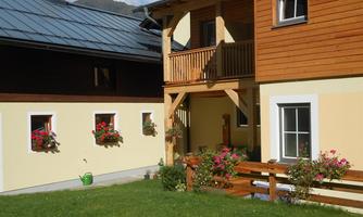 A charming house with wooden siding and a balcony. The garden is decorated with colorful flowers and a green lawn.