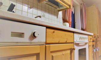 A cozy kitchen with wooden cabinets and a clean countertop. In the background, kitchen utensils and a window can be seen.